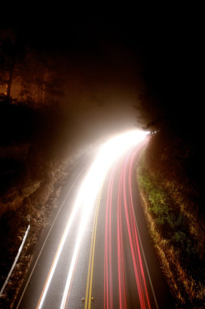 Long exposure showing the blur of passing cars on mountain road on a foggy nightの写真素材