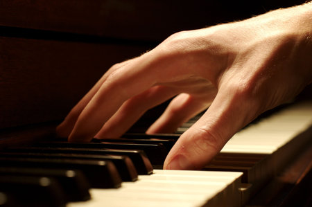 A Caucasian male's hand playing a piano in dramatic lighting