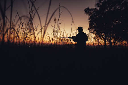 Wide angle shot of hunter standing in long grass with firegun on farmlandの写真素材