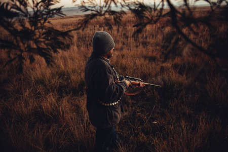 Hunter observing field with gun and cartridge in sunriseの写真素材