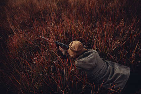 High angle view of Hunter laying in high red grass with rifle aiming on preyの写真素材
