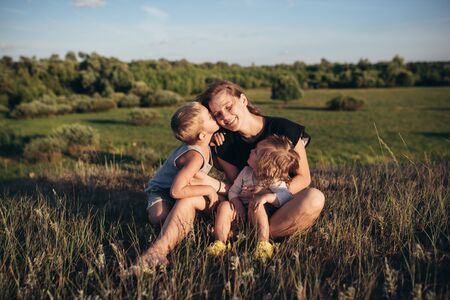Mom with her children resting in nature. The son kisses mom.の写真素材