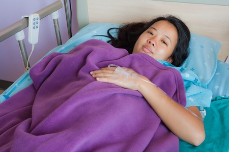 Asian female patient lay down and smile on bed in hospitalの写真素材