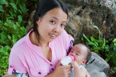 Asian woman feeding her baby and smile  in park from topの写真素材