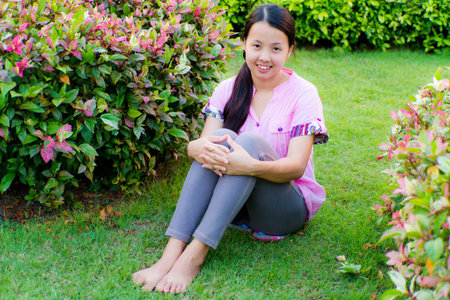 Asian woman sitting and smile in green parkの写真素材