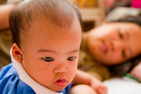 Asian female baby lying on bed with her motherの写真素材