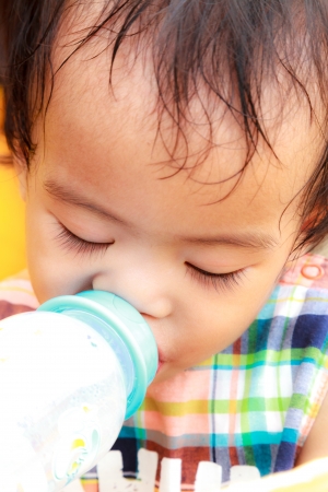 Thai female baby drinking milk from plastic bottleの写真素材