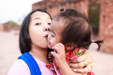 Asian woman holding and kissing her daughterの写真素材