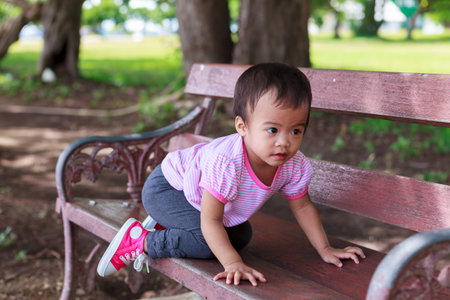 Asian baby girl sitting on wooden bench in parkの写真素材