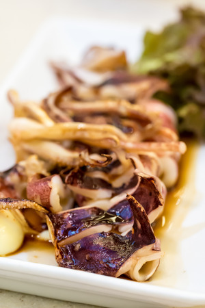 Grilled squid with sauce on white dishの写真素材