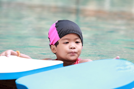 Red dress Asian baby girl playing in swimming poolの写真素材