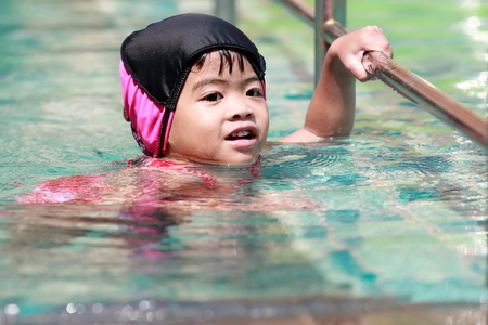 Red dress Asian baby girl playing in swimming poolの写真素材