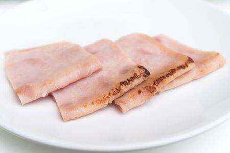 Sliced fried ham on white dishの写真素材