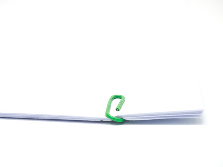 Green paperclip attached on white paper isolated on white backgroundの写真素材