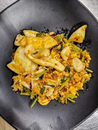Thai cuisine stir squid in salted egg yolk sauce on black dishの写真素材