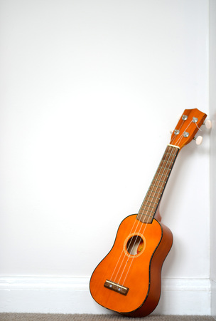 small orange ukelele leaning on white wallの写真素材