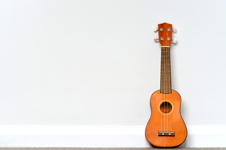 small orange Ukelele leaning on white wallの写真素材