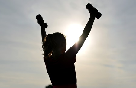 Silhouette of girl exercising and stretching outsideの写真素材