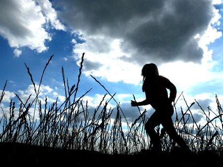 Child running in tall grass with cloudy skyの写真素材