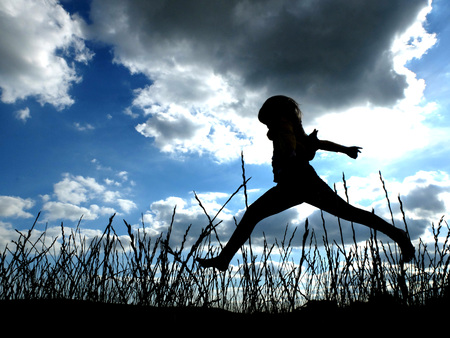 Child jumping in tall grass with cloudy skyの写真素材