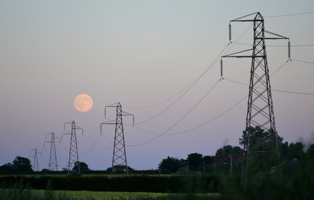 Full moon behind row of electricity pylonsの写真素材