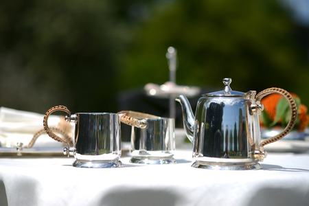 Table set for an English high tea, or afternoon tea, outside with silver teapot and linen tableclothの写真素材