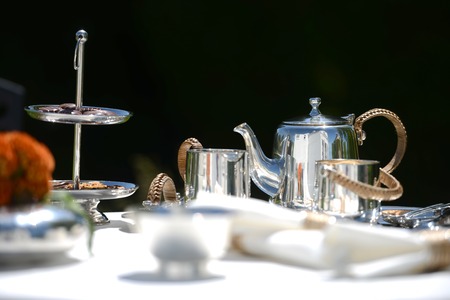 Table set for an English high tea, or afternoon tea, outside with silver teapot and linen tableclothの写真素材