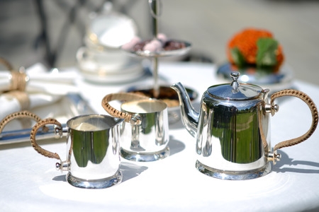Table set for an English high tea, or afternoon tea, outside with silver teapot and linen tableclothの写真素材