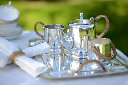 Table set for an English high tea, or afternoon tea, outside with silver teapot and linen tableclothの写真素材