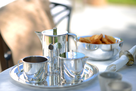 Luxury silver coffee pot on a linen covered table outside in summer.の写真素材