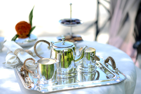 Table set for an English high tea, or afternoon tea, outside with silver teapot and linen tableclothの写真素材
