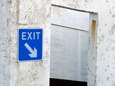 Blue exit sign on a white wall pointing downの写真素材