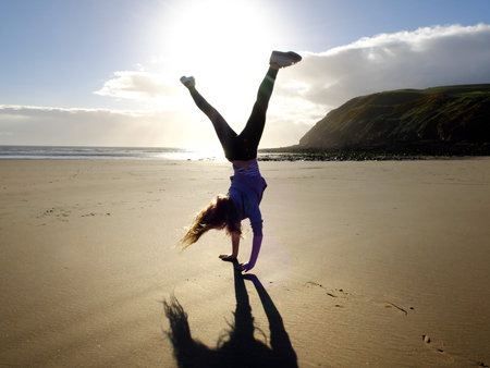 Girl on a sandy beach doing cartwheels at sunset