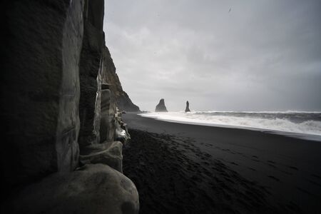 Basalt sea rocks tower over black volcanic sand beach, Reynisdrangar, Iceland.の写真素材