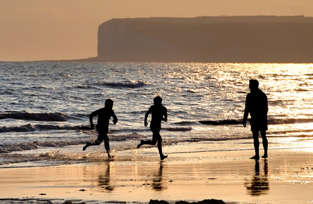 Father and two sons playing ball games on a beach at sunsetの写真素材