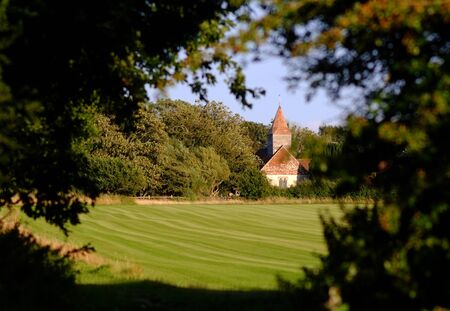 Village church in sun, vignetted by summer foliageの写真素材