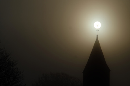 Bird perched on top of a church spire in front of the sunの写真素材