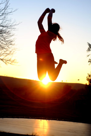 Girl jumping on a trampoline at sunsetの写真素材
