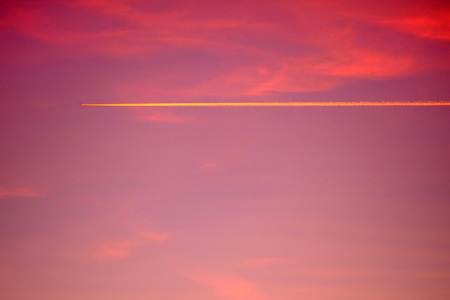Aircraft contrail (condensation trail) illuminated by the setting sunの写真素材