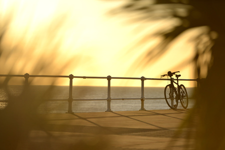 Bike leaning on a railing at Hastings beach, East Sussex, at sunset.の写真素材