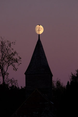 Moon rising behind the steeple of a village church, Chalvington, UKの写真素材