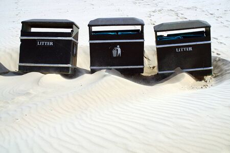Three waste bins on a beach surrounded by sandの写真素材