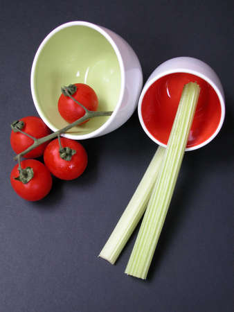 Tomatoes and celery and in red and green bowls on dark gray backgroundの写真素材