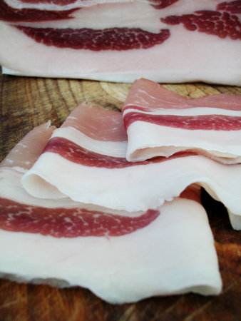 Closeup of a piece of bacon with slices on wood trencherの写真素材