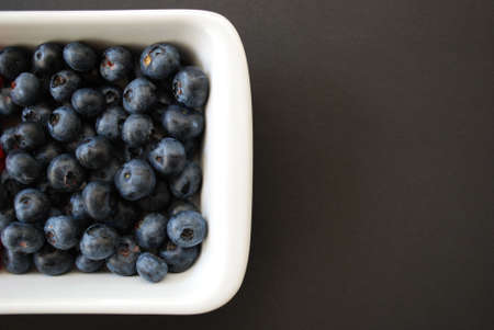 Blueberries in white plate on dark gray background, free space on the rightの写真素材