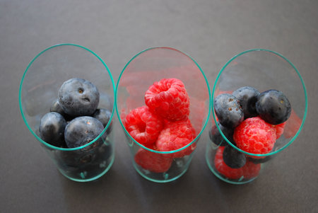 Closeup of blueberries and raspberries in transparent glasses on dark gray background