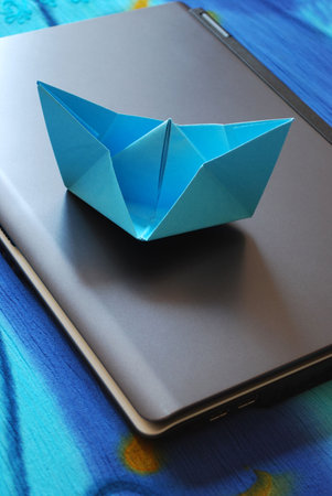 Blue paper boat sailing on laptop, vacation concept, internet surfing concept