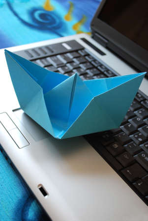 Blue paper boat sailing on laptop, vacation concept, internet surfing conceptの写真素材
