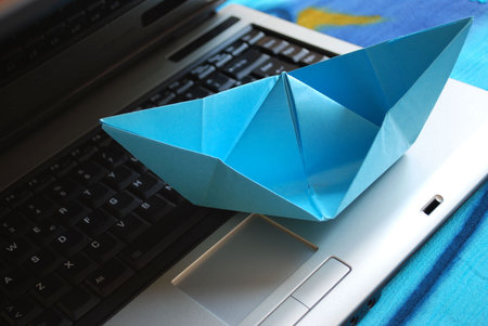 Blue paper boat sailing on laptop, vacation concept, internet surfing concept