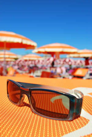 Closeup of sunglasses and beach with orange umbrellas in background, Rimini, Italyの写真素材